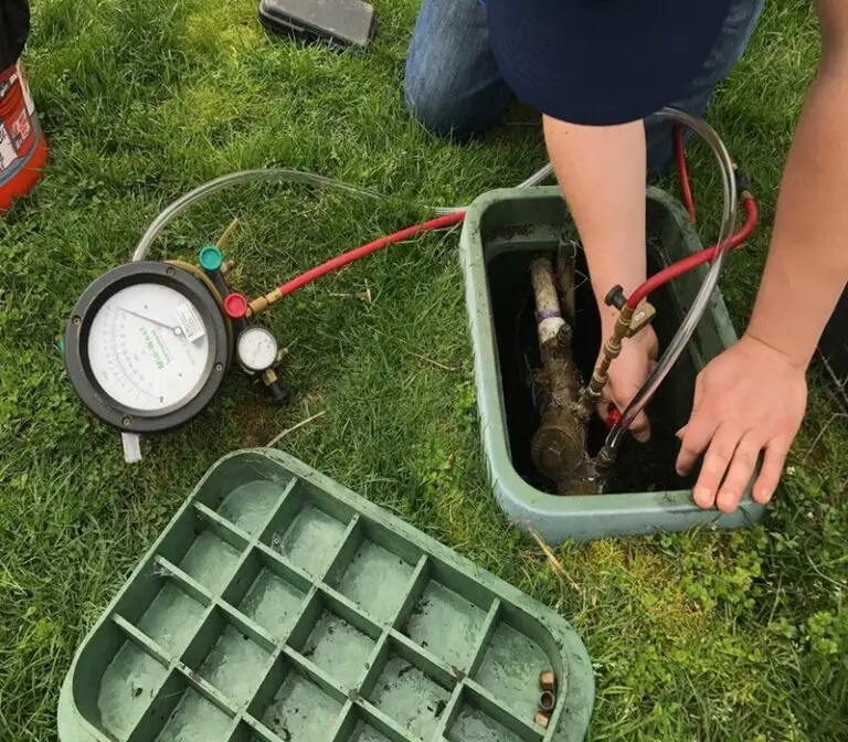 Technician testing a backflow prevention device inside an in-ground valve box