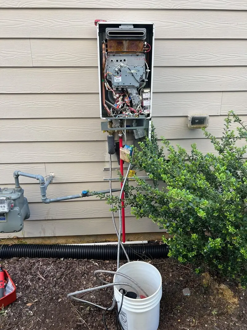 Outdoor tankless water heater being flushed with a pump and bucket