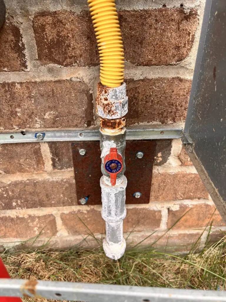 Painted gas piping and shutoff valve below an outdoor tankless water heater