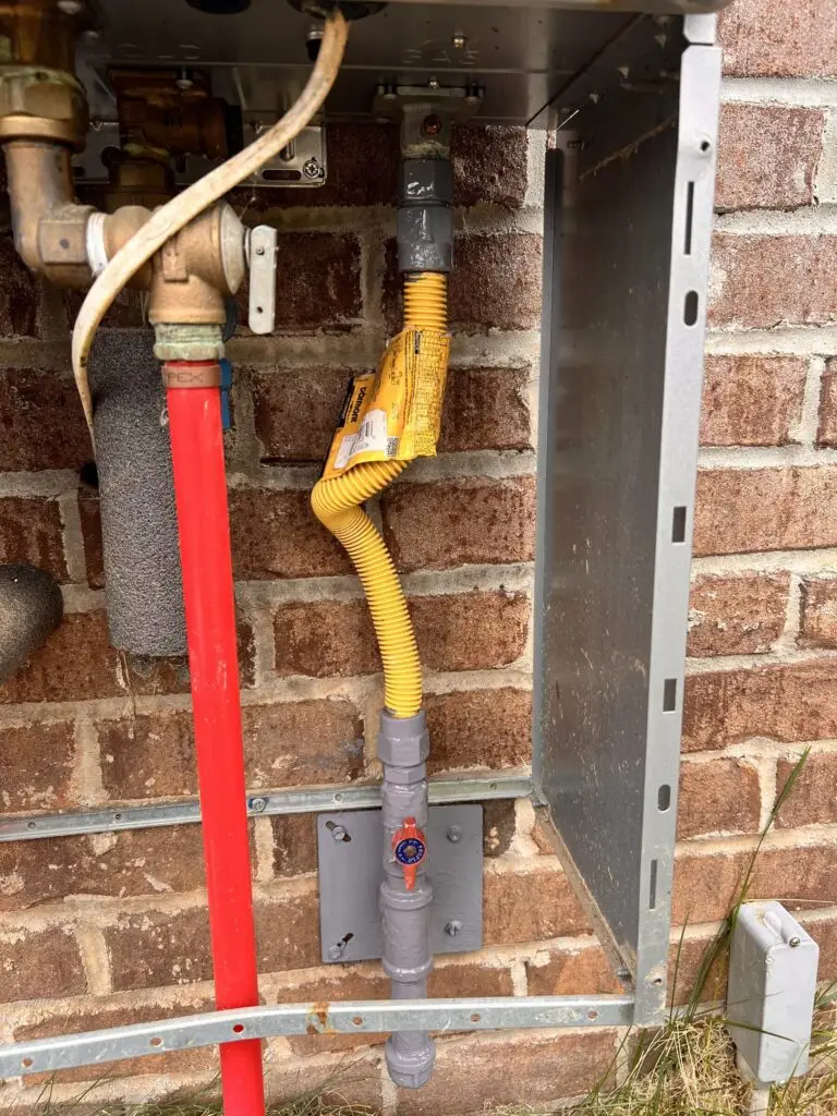 Hot water, cold water and gas connections beneath an outdoor tankless water heater
